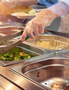 Chef standing behind full lunch service station with assortment of food in trays.