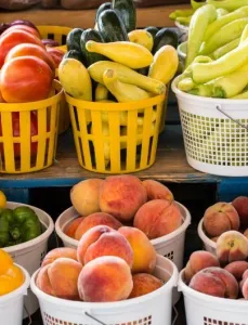 Seasonal produce - baskets of tomatoes, squash, peppers, peaches and other fruit and vegetables for sale in July