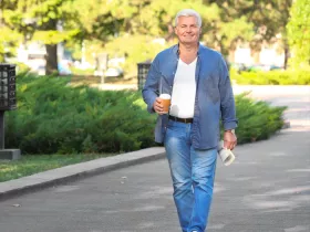 older man walking down street with coffee and paper