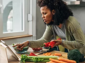 woman checking ipad while cutting vegetables in kitchen