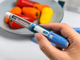 hand holding an obesity medication applicator with bell peppers in the background