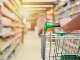 A grocery cart with a green handle in a grocery store aisle