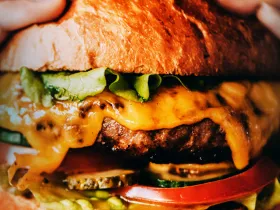 Close up of burger with cheese, pickles, tomato and lettuce.