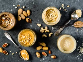 overhead shot of jars of different nut and seed butters with spoons on grey background
