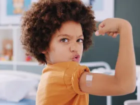 young child flexing muscles showing off a band-aid on their vaccine sight