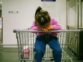 A little girl sitting in an empty shopping cart.
