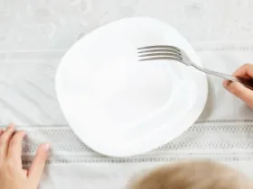 A child holds a fork over an empty plate