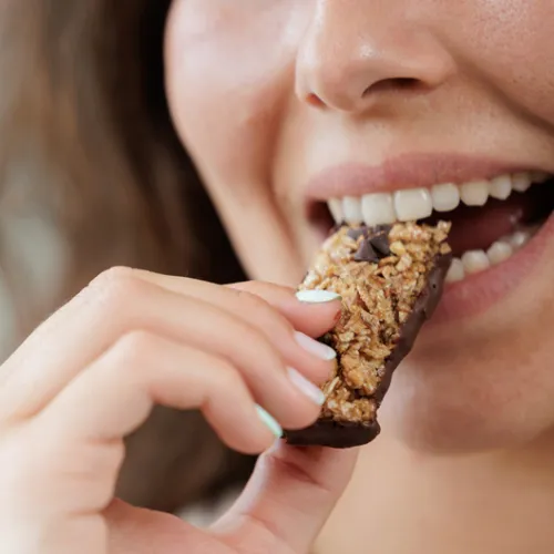 woman taking a bite of granola or protein bar