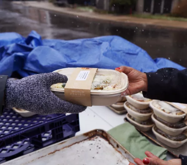 A Make Food Not Waste worker hands a recipient a meal