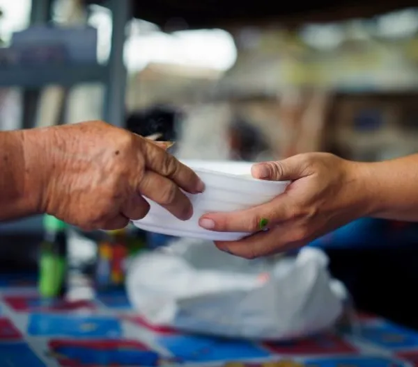 Closeup of a person handing a bowl of food to another person.