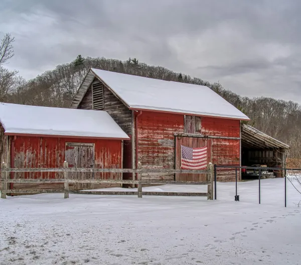 A shabby red barn with an American flag hanging on the side