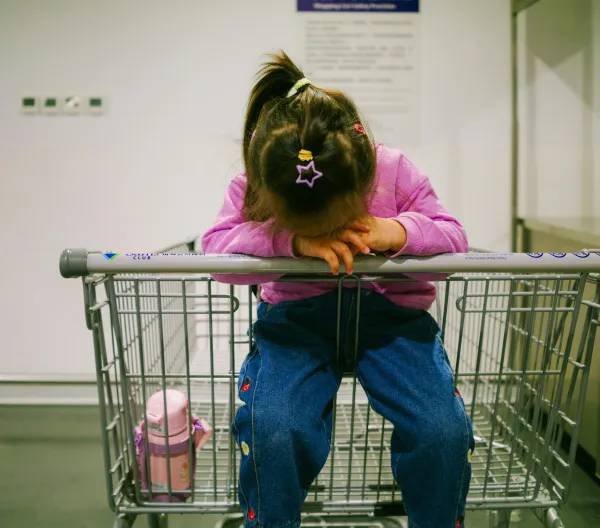 A little girl sitting in an empty shopping cart.