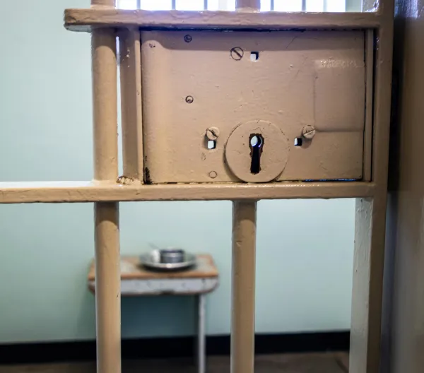 A locked prison cell with a metal food container inside.