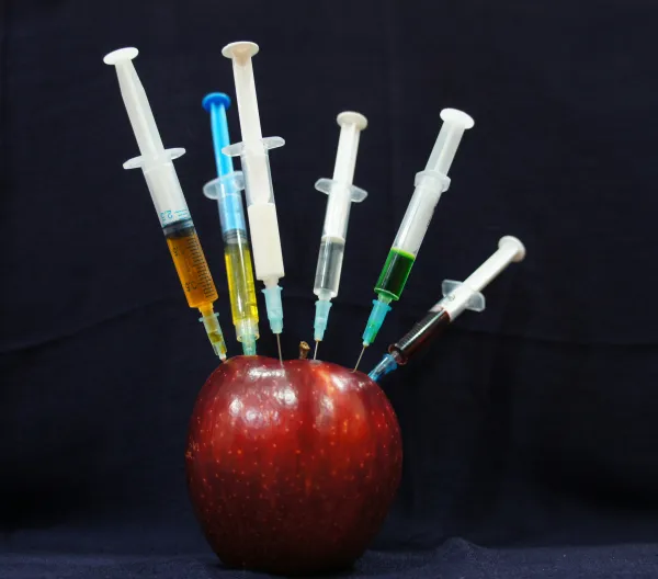An apple with syringes sticking out of it.