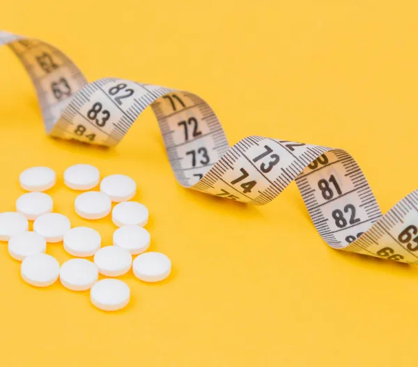 A measuring tape and weight loss pills on a yellow background