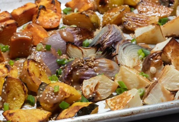 chopped winter vegetables sprinkled with sesame seeds and scallions roasted on baking sheet