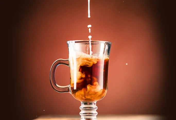 mug of coffee with creamer being poured in