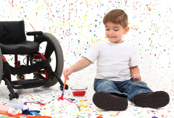 Child sitting on the floor next to wheelchair and playing with paint
