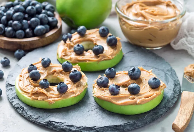 Plate with green apple slices covered in peanut butter and sprinkled with blueberries