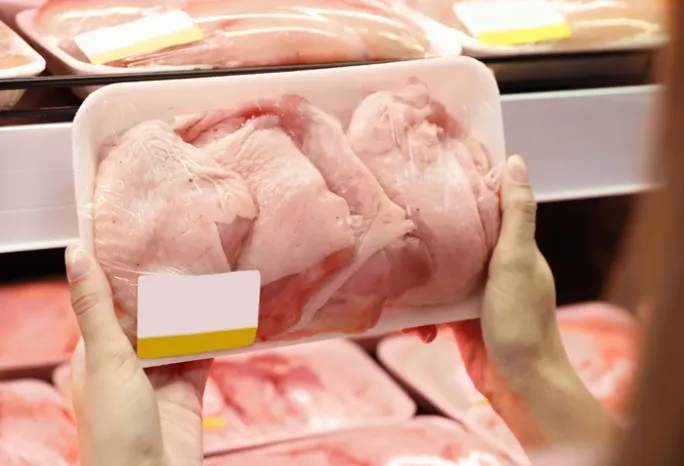 person holding a package or raw chicken in front chicken shelf at supermarket