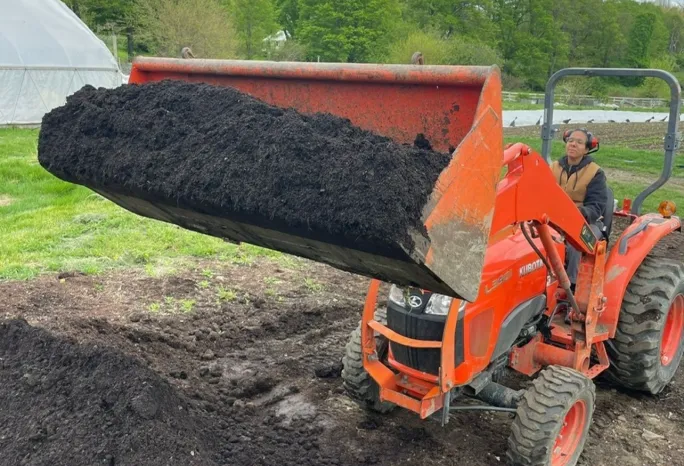 A farmer on a tractor lifting dirt from a large pile