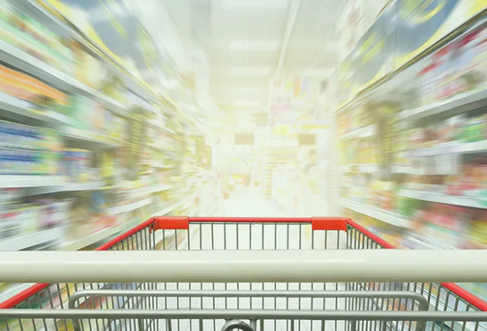 grocery cart in focus in the foreground with grocery store shelves out of focus in the background