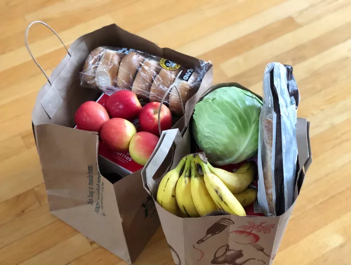 Two paper grocery bags full of apples, bananas, cabbage, and bread products