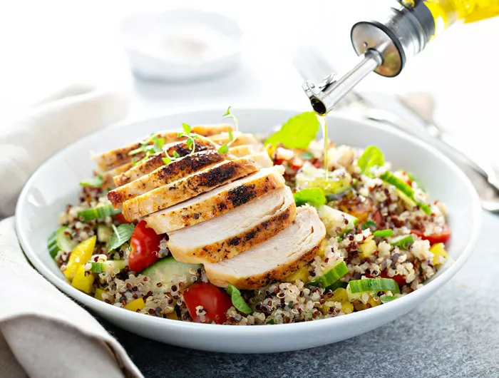 bowl of salad topped with chicken with olive oil drizzled on top