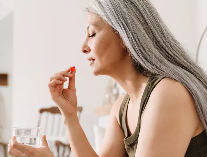 woman holding a glass of water and red supplement close to her mouth