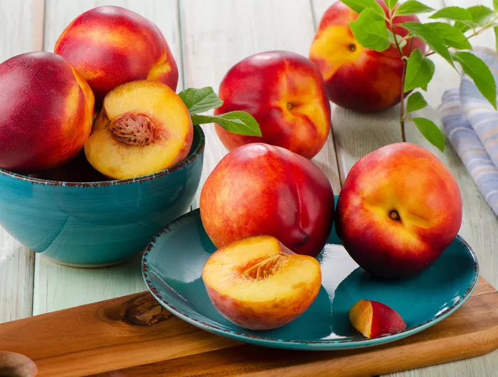 a blue bowl filled with nectarines next to a blue plate of nectarines