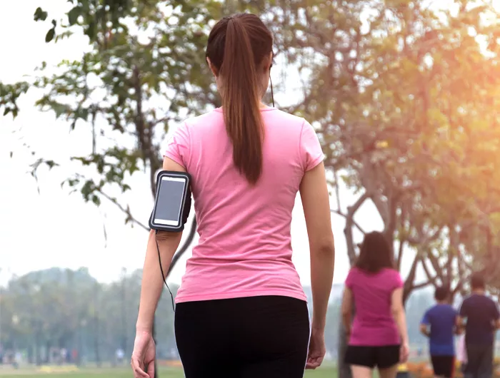 woman in a pink shirt walking away from  the camera and waring a phone holder on her arm