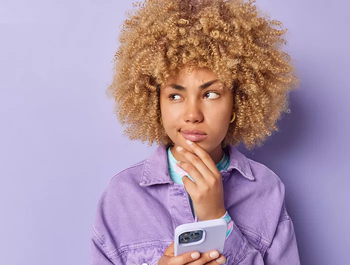 person in purple shirt with purple background holding a phone and holding their chin