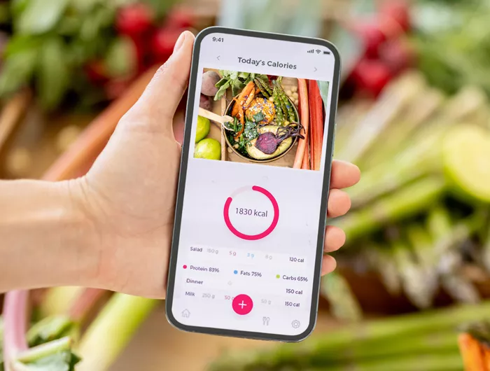 hand holding a phone with food tracker on the screen and vegetables in background