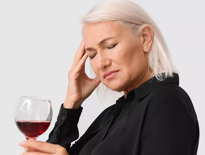 woman holding her head and a glass of red wine