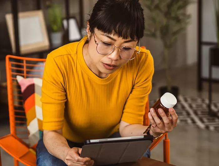 Woman in yellow shirt reading a supplement label and reading on an ipad