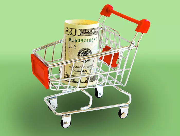 roll of cash in a shopping cart on green background
