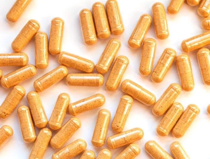 Capsules of yellow powder scattered on a white background