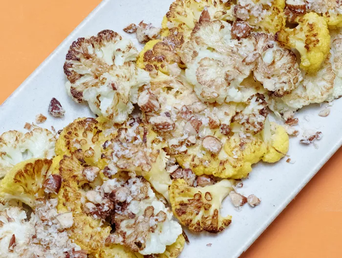 white plate of roasted cauliflower on an orange background