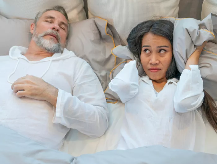 one person sleeping soundly and the person next to them shielding their ears with a pillow