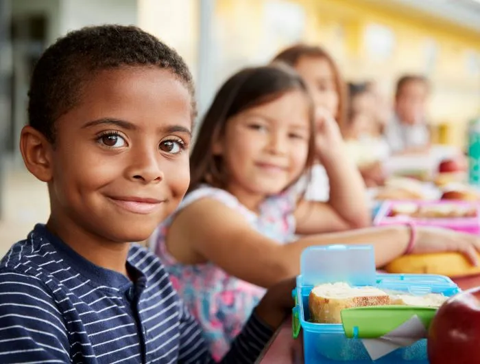 Young students enjoy a healthy, dye-free school lunch at a table and smile at camera