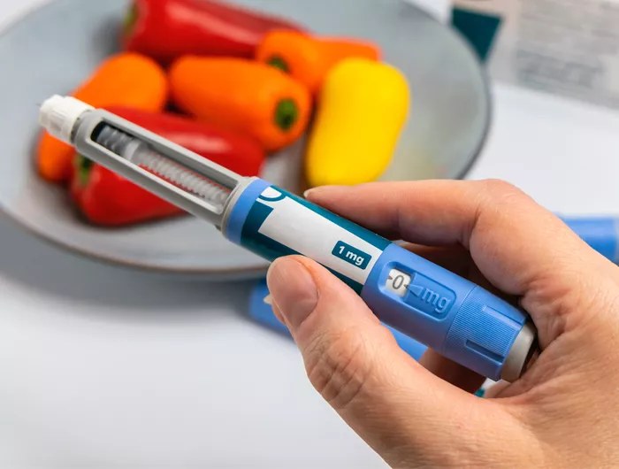 hand holding an obesity medication applicator with bell peppers in the background