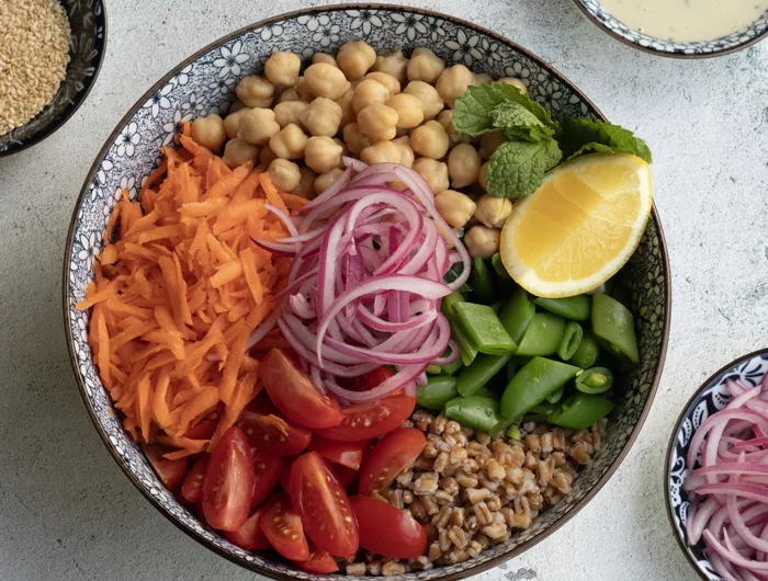 bowl filled with un-mixed vegetables like shredded carrots, red onion, chickpeas, and more