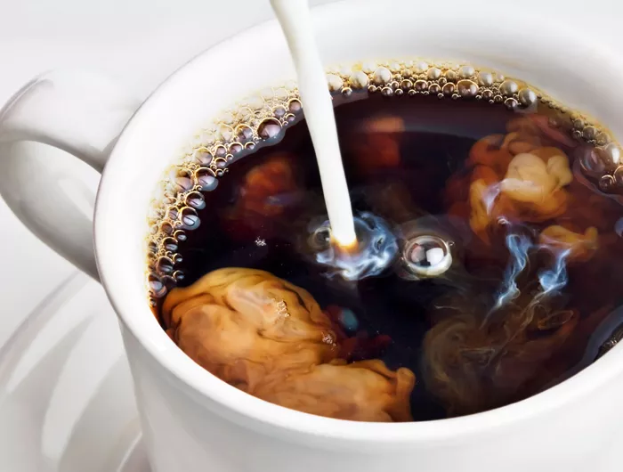 cup of coffee with creamer being pored in