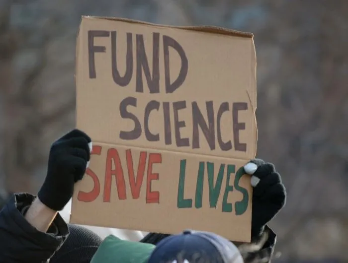 A protest sign reads "FUND SCIENCE SAVE LIVES"