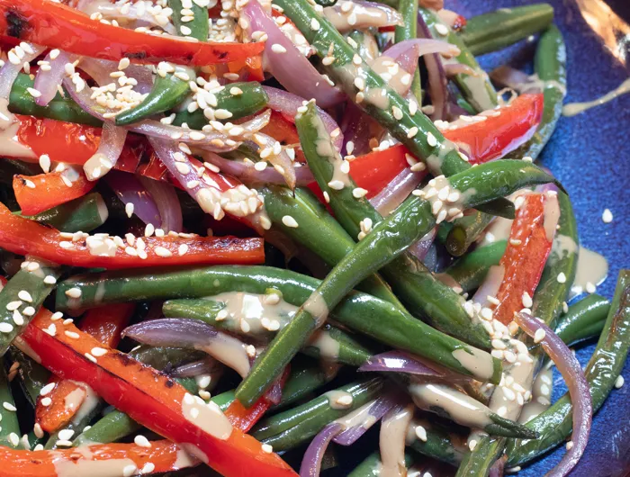 green beans and sliced peppers covered in sauce and sesame seeds