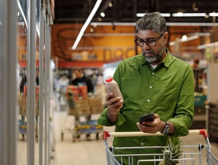A man ina  green shirt reads the label on a packaged food product in a grocery store