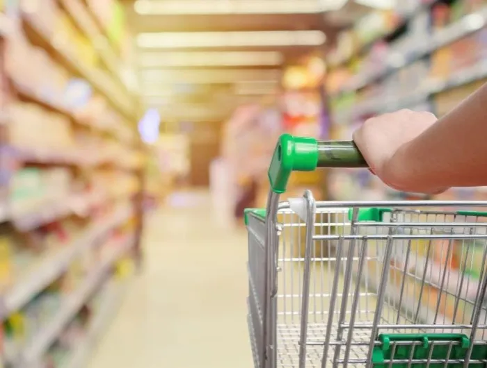 A grocery cart with a green handle in a grocery store aisle