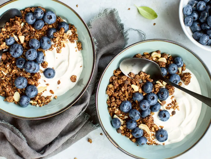 two blue bowls filled with yogurt, granola and blueberries
