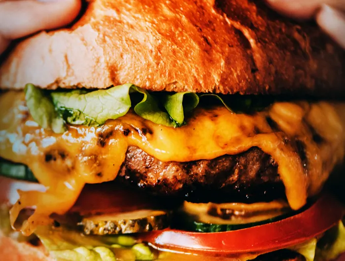 Close up of burger with cheese, pickles, tomato and lettuce.