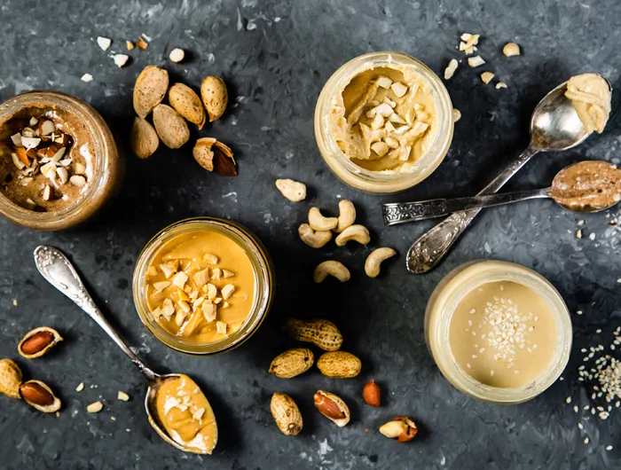overhead shot of jars of different nut and seed butters with spoons on grey background